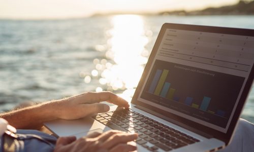 Senior man working on his laptop lying on deck chair on the beach during sunset