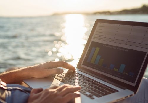 Senior man working on his laptop lying on deck chair on the beach during sunset